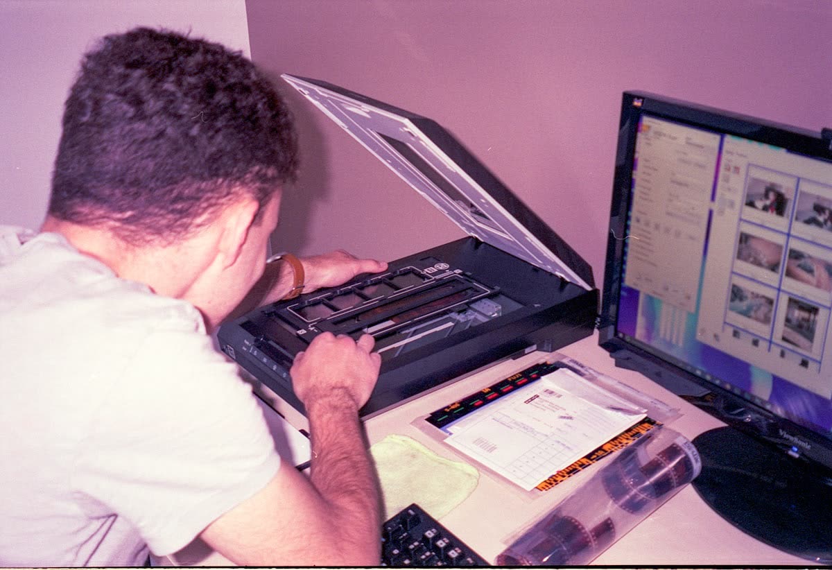 Person placing a document on a flatbed scanner beside a computer