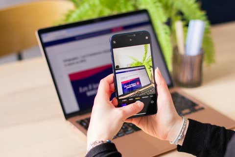A person holding a cell phone in front of a laptop